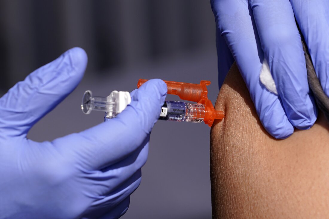 A gloved worker holding a syringe administers a vaccine to a patient.