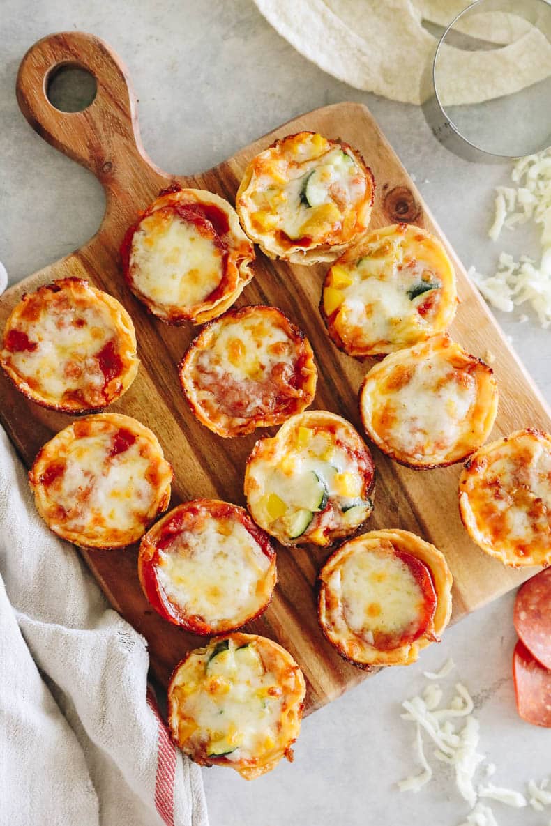 mini tortilla pizzas on a brown cutting board.